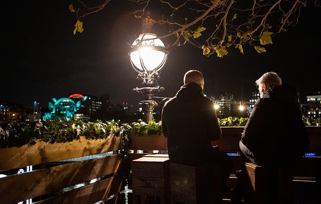 Two people sitting on a bench at night with a lamp post in the background, captured at 3UP Rooftop Bar.