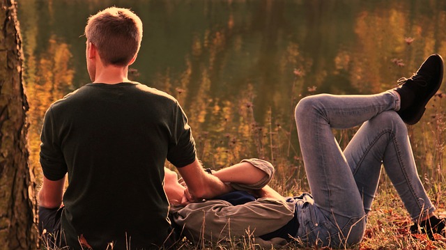 A couple enjoying a serene lakeside moment, sitting on the ground. 